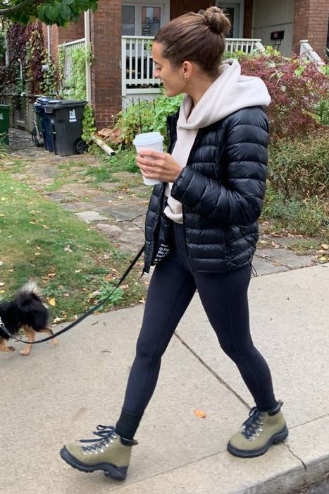 A model strolling with a small dog, wearing a puffer jacket and green lace-up boots, perfect for a guide on casual outdoor looks