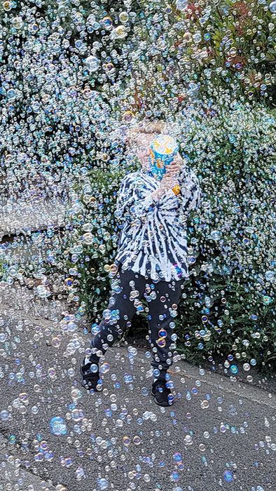 A child is playfully hidden behind a cloud of bubbles created by the bubble machine.