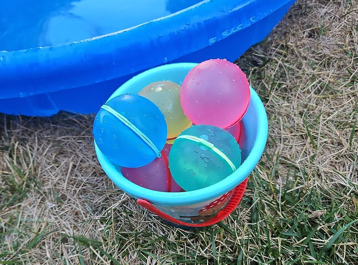 A reviewer's photo showcasing a bucket filled with reusable water balloons, set up outside for a fun day of water play.