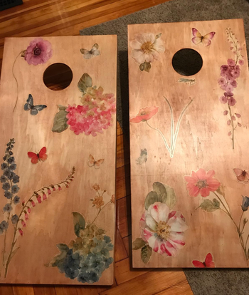 There are two cornhole boards, each featuring intricate floral and butterfly patterns.