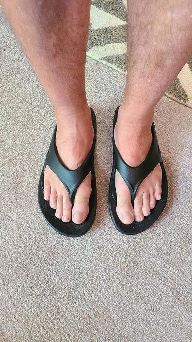 A person wearing basic black flip-flops standing on a patterned carpet.