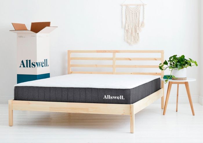 The Allswell mattress rests on a wooden bed frame, with an Allswell box placed next to it.