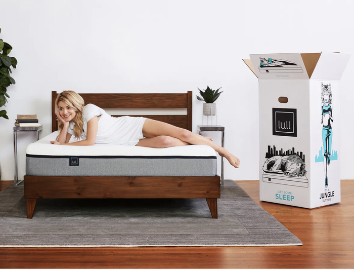 A person lying on a Lull mattress, with the box placed beside it.