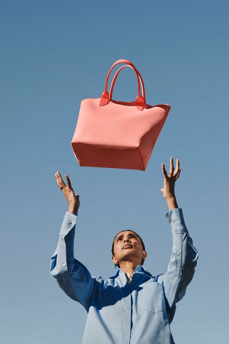 a model tossing a bright orange tote bag in the air with excitement