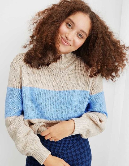 a model wearing a tan sweater with a blue stripe across the chest