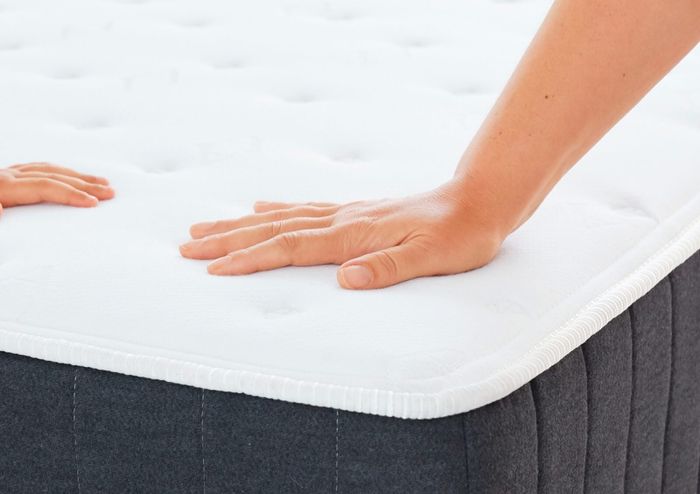 A model's hands press down on the Allswell mattress to demonstrate its comfort.