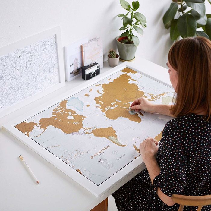 A traveler marking off the destinations they've visited on a gold scratch-off map.