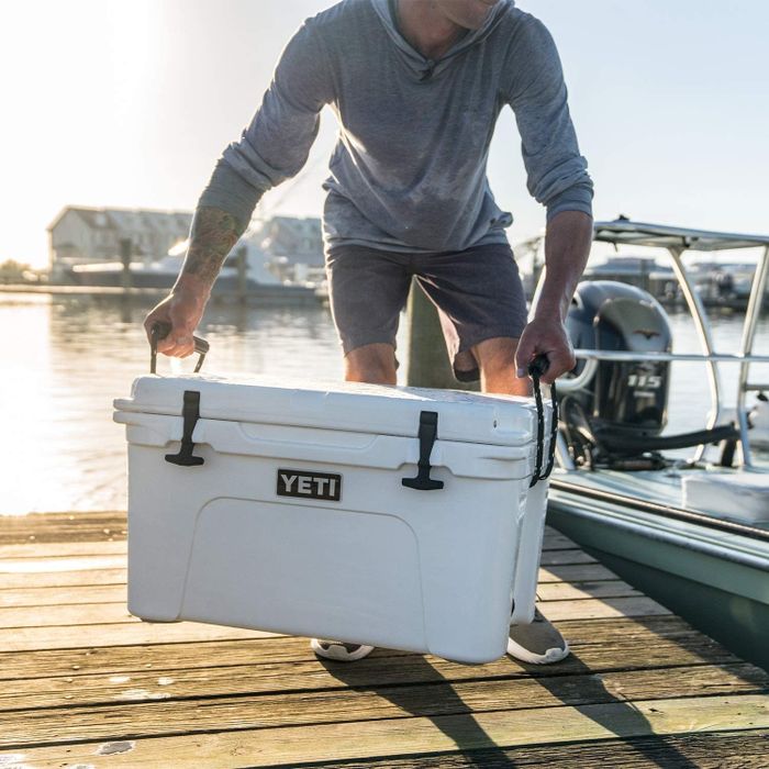 A person carrying a durable cooler along a boat dock, ready for a day on the water.