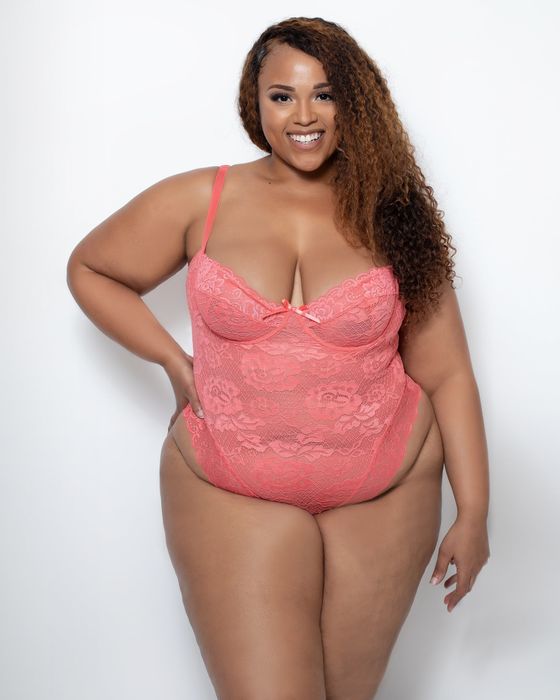 A plus-size model confidently wearing a pink floral lingerie set.