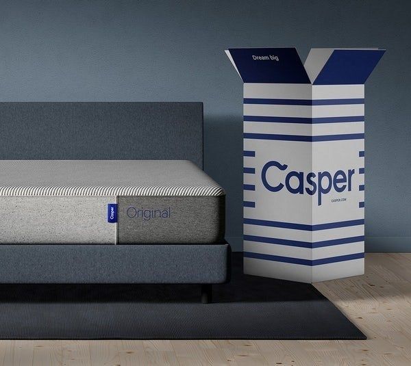 A Casper mattress placed on a bed frame, with a Casper box positioned to the right.