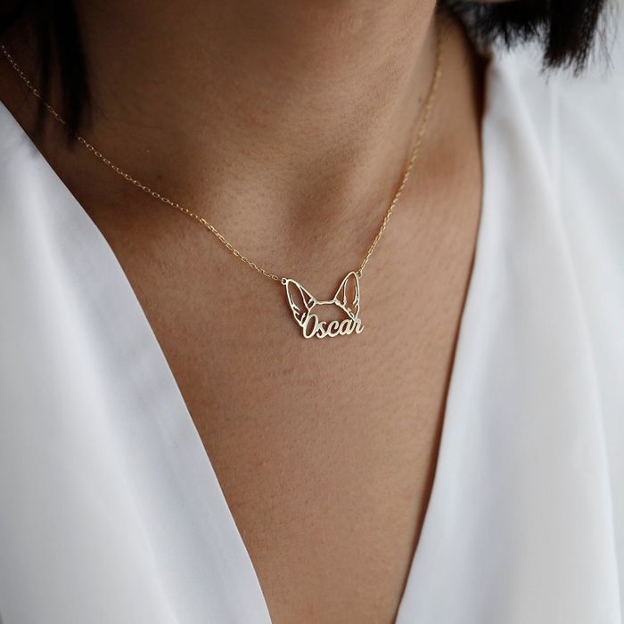 A model is seen wearing a gold necklace with dog ears and their pet's name on it.