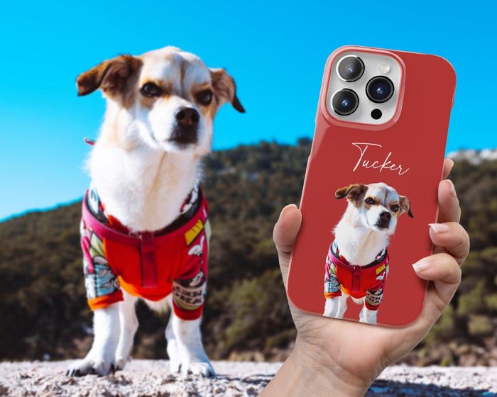 A person holding a phone with a red case featuring a dog design, with the actual dog visible in the background