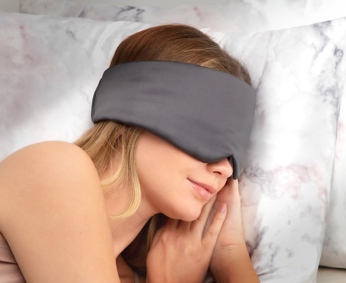 A model is shown wearing the grey eye mask, which wraps around the head, eliminating the need for an elastic band.