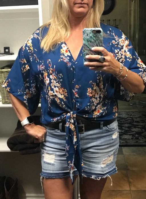 A reviewer styled in the shirt in blue with a vibrant multicolor floral print paired with denim shorts