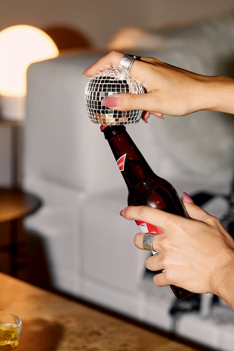 A model demonstrates how to use the bottle opener, which is designed as a disco ball with the opener placed on the bottom, to easily open a beer.
