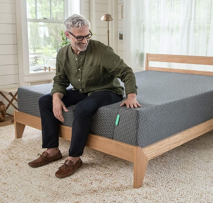 A model lounging on the charcoal-colored mattress placed on a wooden bed frame