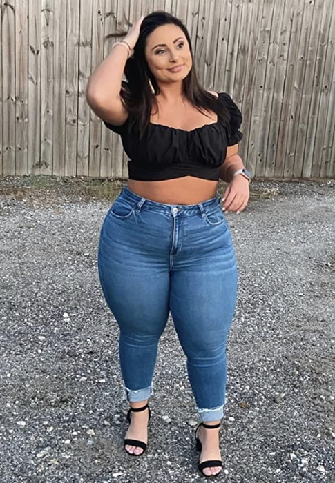 A reviewer wears a black top paired with jeans and black heels.
