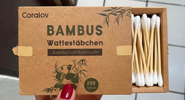 A reviewer photo showing a hand holding a partially open cardboard box, revealing bamboo cotton swabs inside.