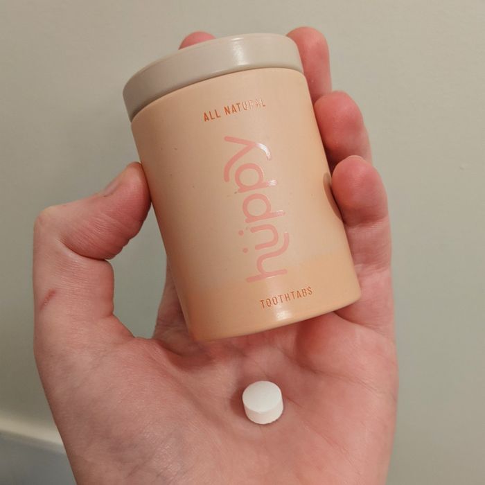 A hand holding a pink tin and a white tab.