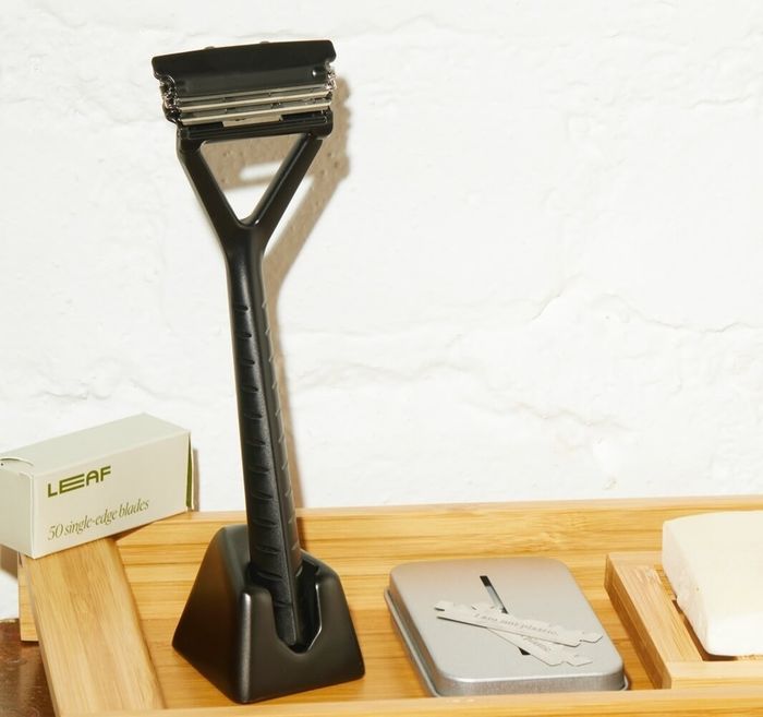 A black metal razor placed in a stand next to a tin and several blades.