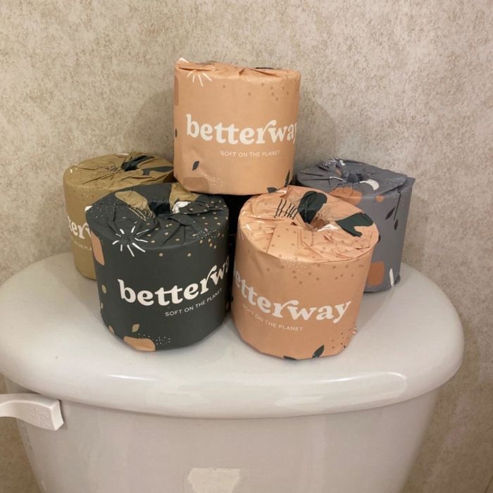 A reviewer's photo showing the back of a toilet stacked with several individually wrapped rolls of toilet paper.