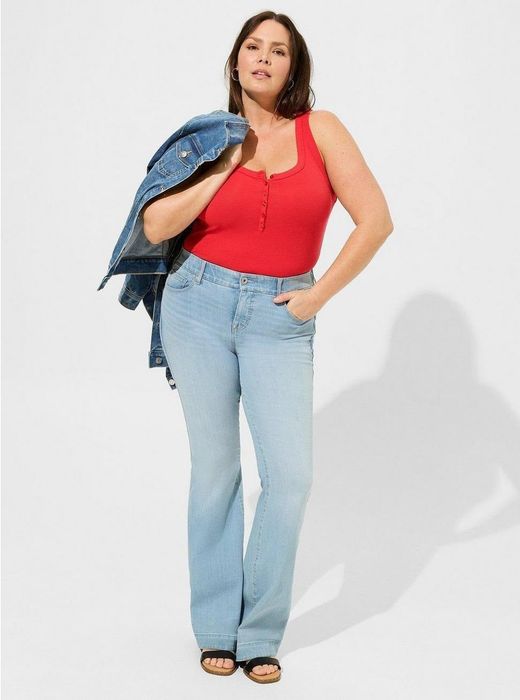 Woman dressed in a red tank top, light blue jeans, and sandals, holding a denim jacket over her shoulder.