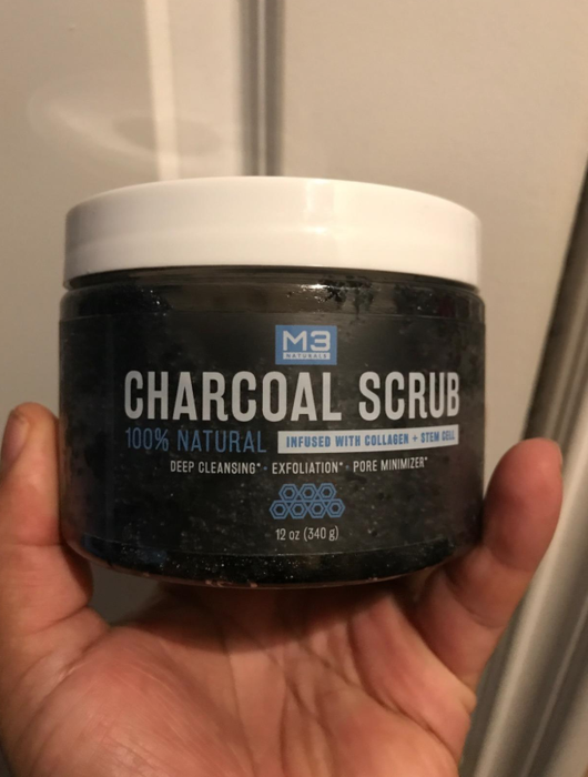 A reviewer's photo showing a hand holding a tub of the charcoal body scrub.