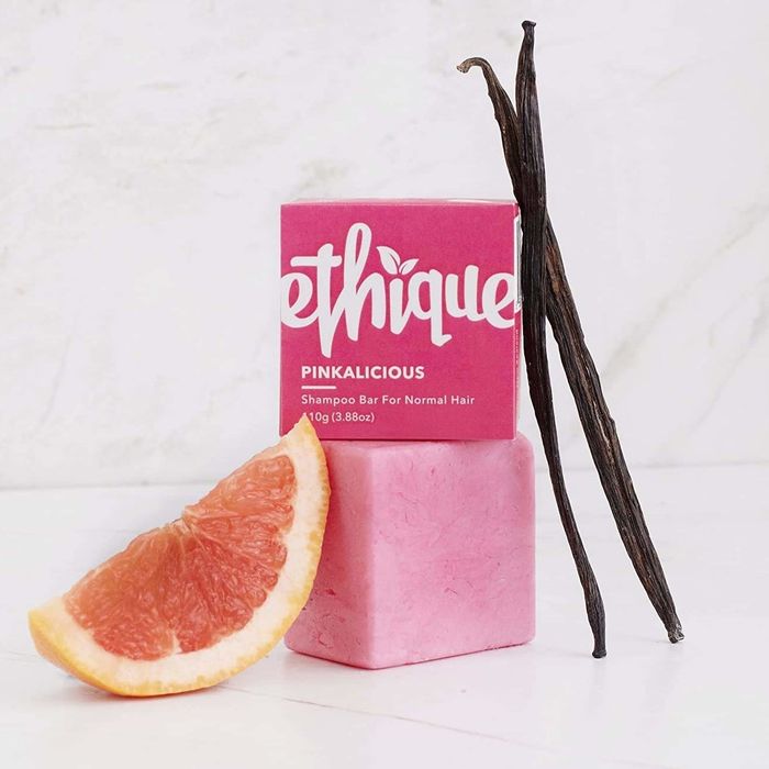 The pink Ethique shampoo bar packaging placed beside a pink square shampoo bar and a slice of grapefruit.