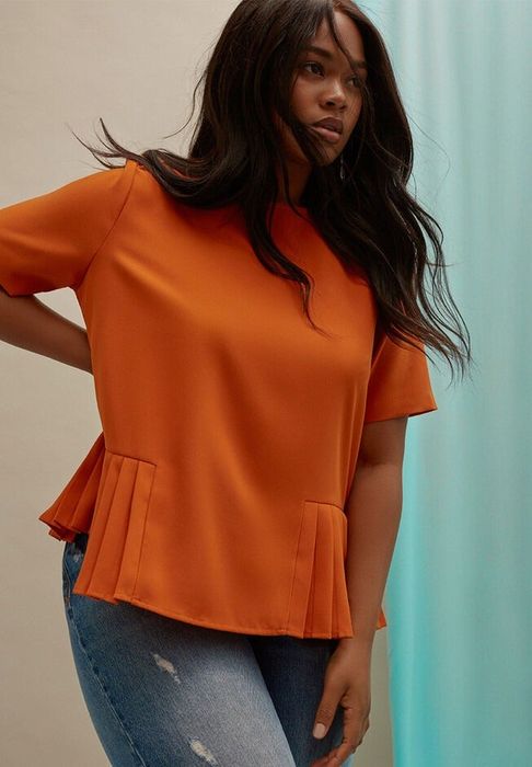 Model posing in an orange peplum top and jeans.