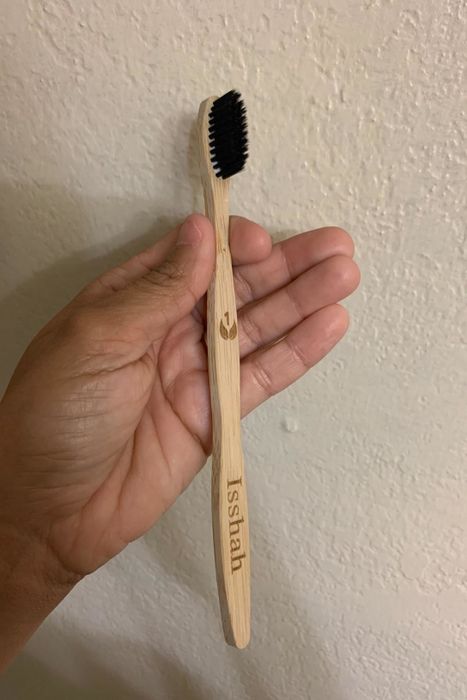 A reviewer's photo featuring a hand holding a bamboo toothbrush with black bristles, engraved with the number one.