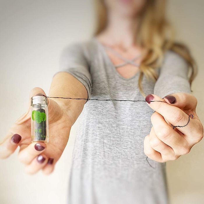 A model holding a glass tube filled with dental floss and pulling out a long strand of floss.