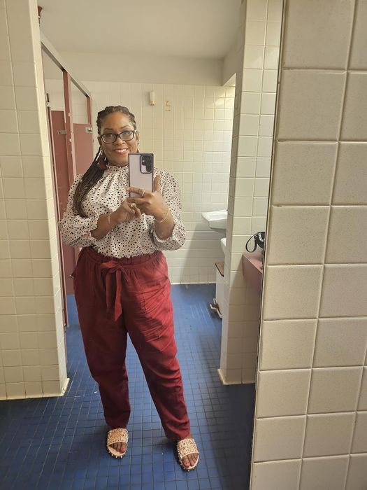 Woman in a mirror selfie, wearing a polka dot top, maroon pants, and coordinating sandals.