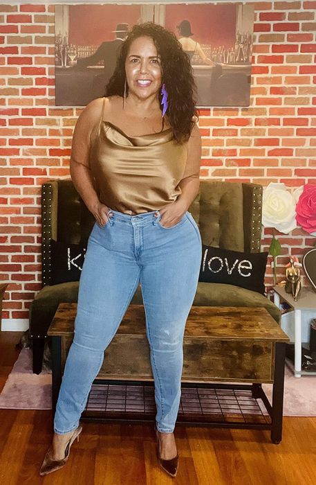 Reviewer standing in a room wearing a gold satin cowl neck top, paired with jeans and pointed-toe shoes.