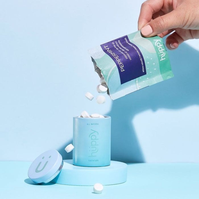 A hand pouring tablets from a pouch into a blue tin.