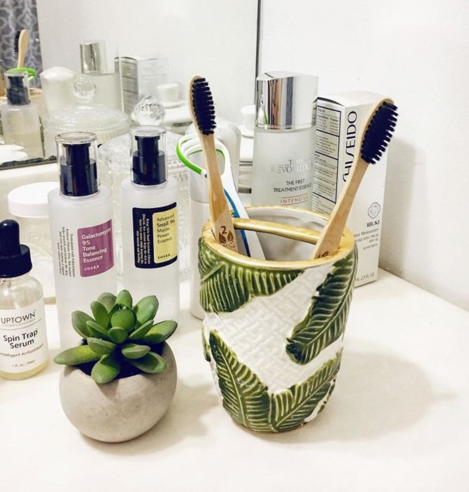 A reviewer's photo showing two bamboo toothbrushes placed in a leaf-printed cup on a bathroom countertop.