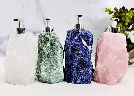 A set of four soap dispensers, each made from rough-cut stones in different colors, topped with stainless steel pumps.