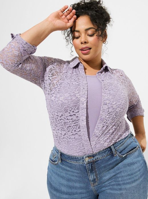 A person poses in a purple lace shirt paired with denim jeans, gazing to the side.