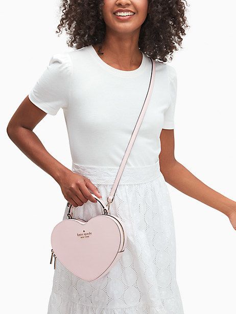 A model is seen holding a light pink, heart-shaped Kate Spade bag.