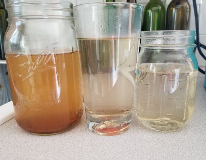 A glass on the left with brown water, a glass in the center filled with cloudy water, and a glass on the right containing clear water