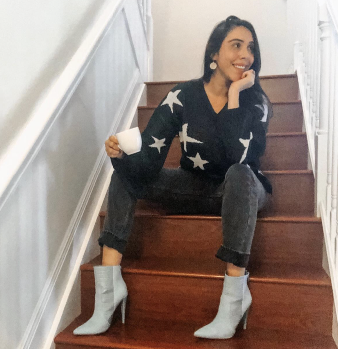 reviewer showcasing the star sweater while perched on a staircase