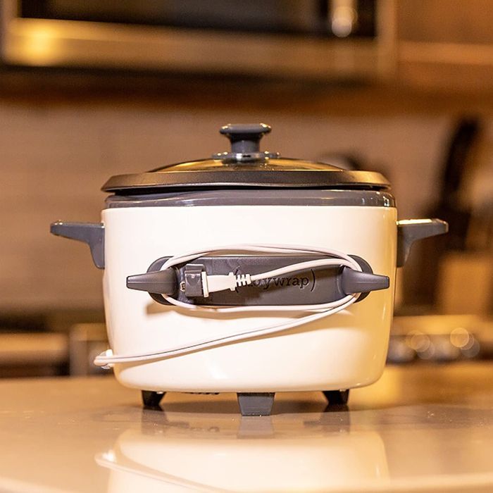 A gray, oval-shaped rubber adhesive with two prongs attached to a slow cooker, with the cord neatly wrapped around it