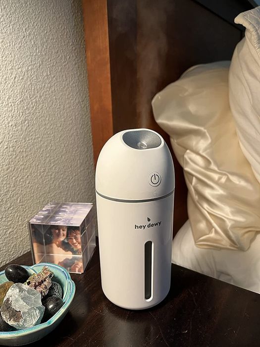 A sleek, white Hey Dewy humidifier releases a steady stream of water vapor from its top, perfect for refreshing your skin.
