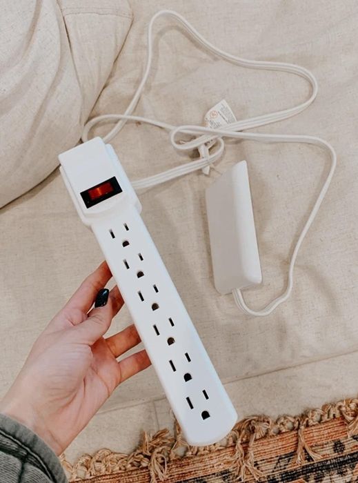 A reviewer’s photo showing a hand holding the socket cover with the attached power strip.