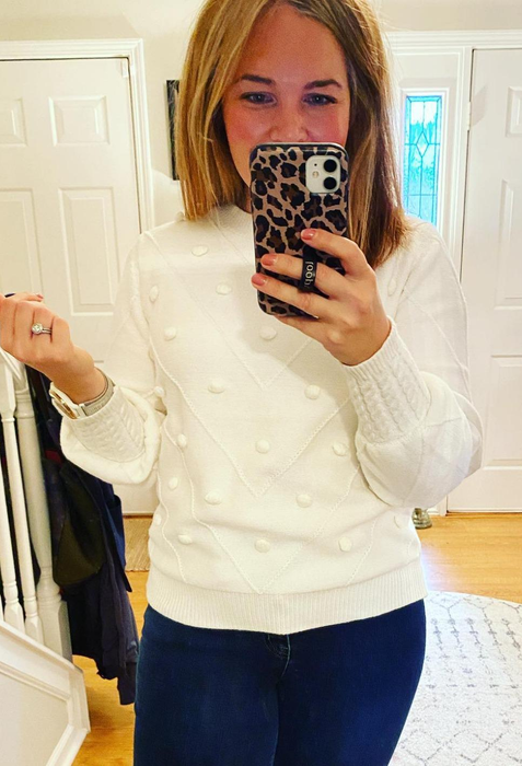 A reviewer wearing the white pom-pom sweater paired with jeans