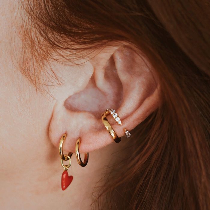 The model is wearing gold heart charm earrings.