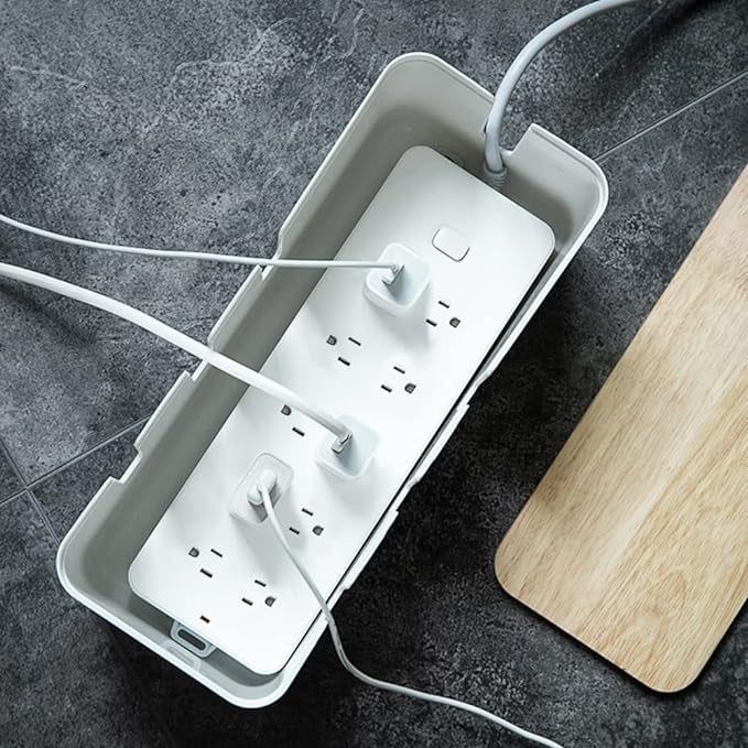 A power strip with multiple plugs connected, placed inside a rectangular container, with a wooden lid placed nearby.