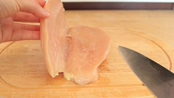 A chicken breast that has been sliced horizontally, with the top portion being lifted by a person.