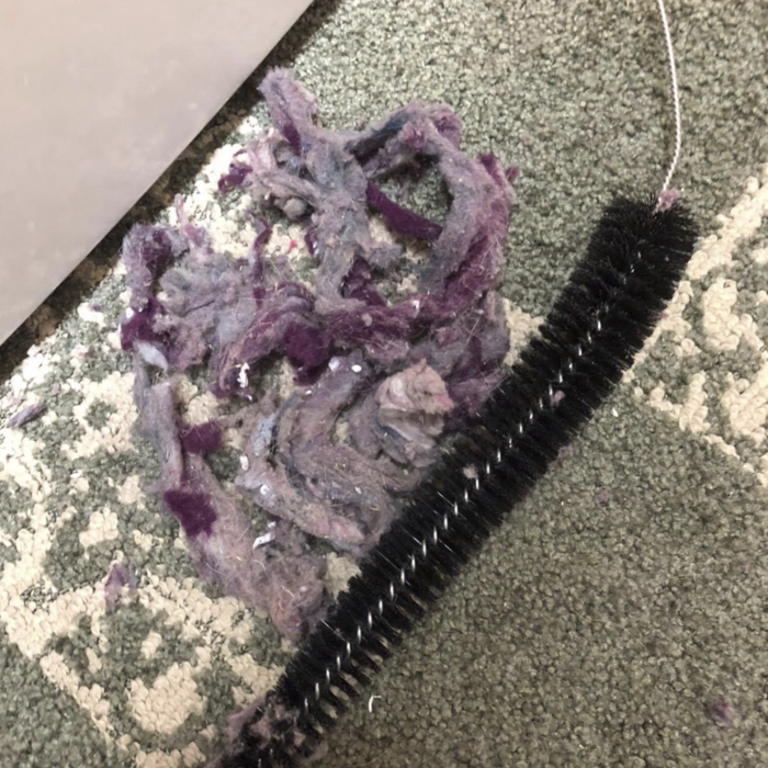 A pile of dust and debris with the brush next to it, pulled out of the dryer vent by the reviewer.