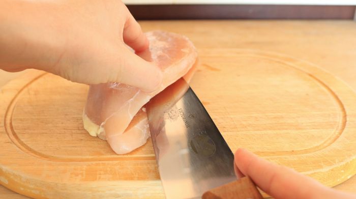 A knife cutting horizontally halfway through a chicken breast.