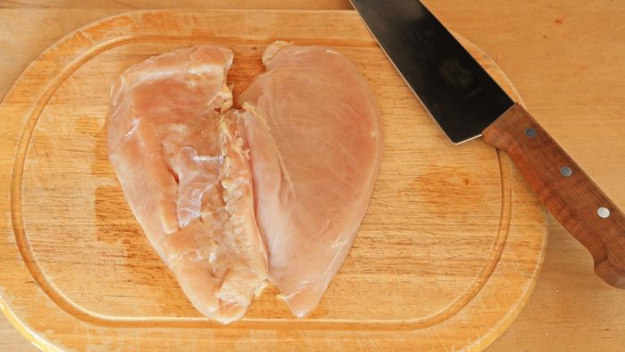 A raw chicken breast butterflied on a cutting board next to a carving knife.